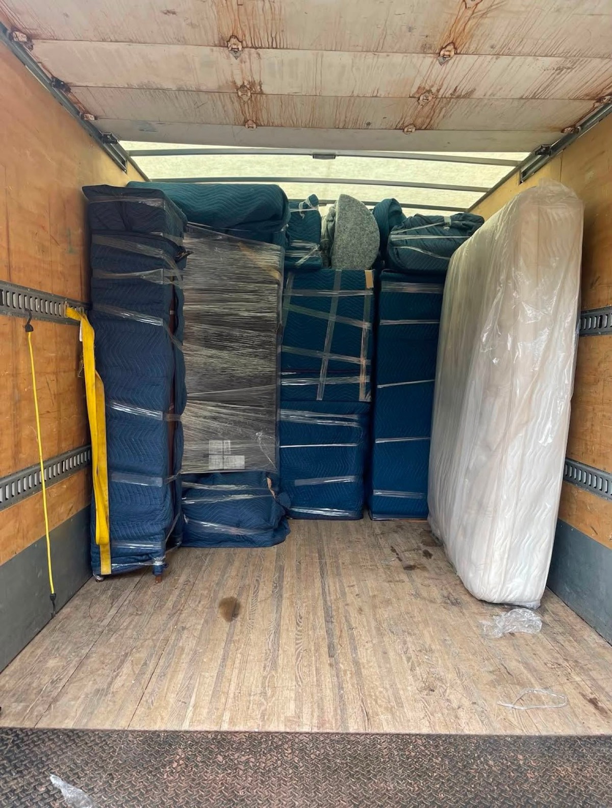Intérieur d’un camion avec des meubles couverts et un matelas emballé.